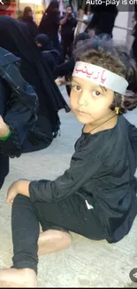 Child in traditional gathering, sitting on the ground.