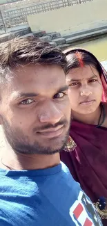 A couple taking a selfie near a serene river with traditional attire.