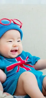 Cute baby wearing blue with red accents sitting happily.