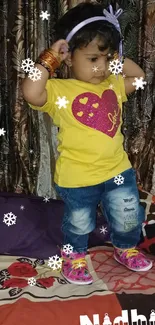 Adorable baby in yellow heart shirt standing on bed.