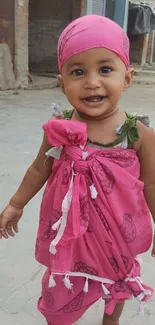 Smiling baby in pink outfit standing outdoors.