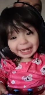 Smiling baby in pink pajamas wearing headphones, joyful expression.