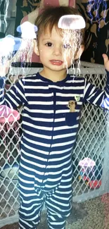 A cute baby in navy and white striped pajamas standing indoors.