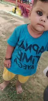 Cute baby in blue T-shirt and yellow shorts standing outdoors.