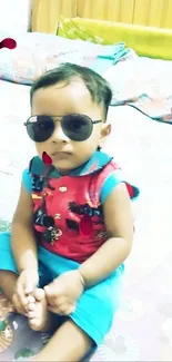 Adorable baby wearing sunglasses on a colorful bed.