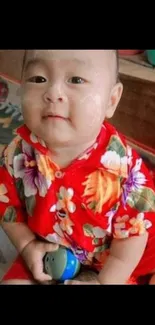 Baby in red floral shirt playing joyfully.