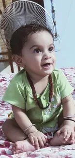 Adorable baby in green outfit smiling on floral bed.