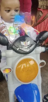 Cute baby in festive attire on a toy motorcycle.