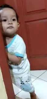 Adorable baby peeking behind red door, smiling.