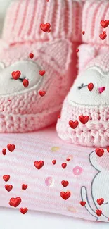 Pink knitted baby booties on stacked clothes.