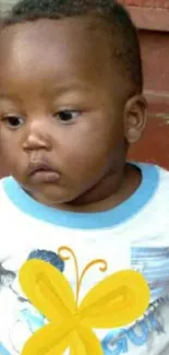 Cute baby wearing a butterfly shirt on a brown background.