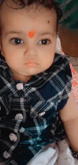 Baby with tilak in checkered shirt, expressive eyes and cute smile.