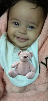 Smiling baby in pink outfit holding a teddy bear.