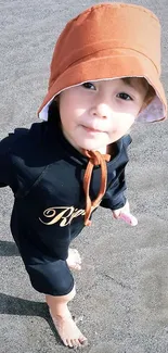 Adorable baby with orange hat on sandy beach.