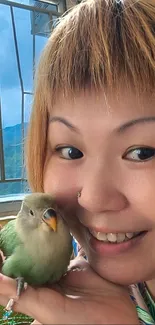 Smiling person holding a cute green bird.
