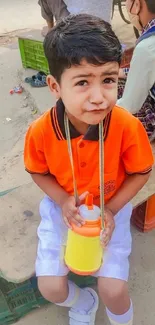 Young boy in orange shirt with a juice cup.