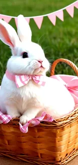 White bunny in a wicker basket with a pink bow, on a grass picnic setting.