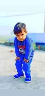 Young child in blue outfit posing outdoors on a sunny day.