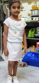 Adorable child standing in a cozy kitchen setting, wearing a white outfit.