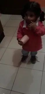 A cute child wearing a pink sweater in a room with brown tiles.