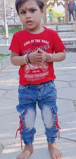 Young child in a red shirt and blue jeans poses outdoors.