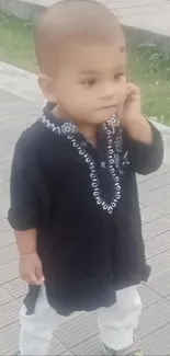 Toddler in black traditional outfit outdoors.