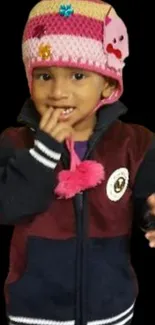 Child wearing a colorful winter hat and jacket on black background.