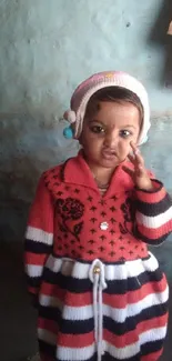 Cute child in a striped winter outfit against a blue wall.