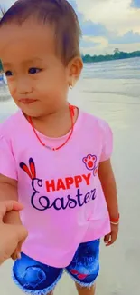 Child in pink shirt holding hands on the beach.