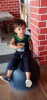 Child sitting on a ball with a red brick wall background.