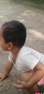 A cute child crouching on a sunlit pathway, in a natural outdoor setting.