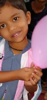 A smiling child holding a pink balloon, creating a joyful scene.