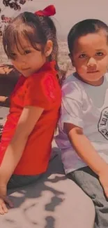 Two children sitting outdoors, one in red.