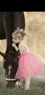 Little girl in pink dress hugging a horse on a grassy field.