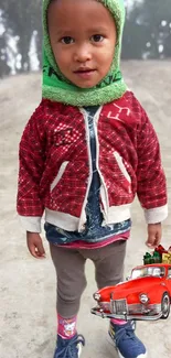 Cute child in red jacket with green scarf and vintage car toy.