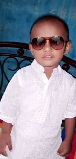 Cute child wearing sunglasses and white attire in a vibrant setting.