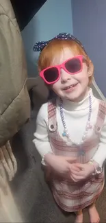 Child in plaid dress and pink sunglasses.