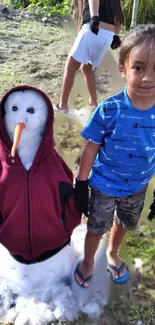 A cheerful child stands beside a snowman wearing a red jacket outdoors.