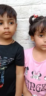 Two children wearing cartoon shirts against a white brick wall.