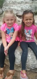 Two cute kids in pink shirts sitting on rocks.