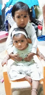 Two children sitting on a chair with playful expressions.