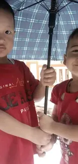 Two cute kids in red shirts under an umbrella, smiling and playing together.