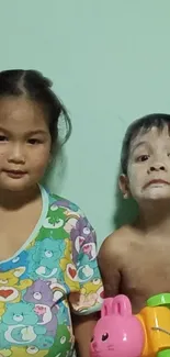 Two adorable kids smiling with playful toys against a light green backdrop.