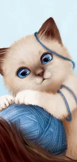 Cute kitten with blue eyes and yarn ball on a sky blue backdrop.