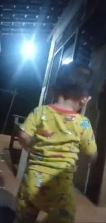 Child in bright pajamas walking indoors at night.