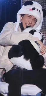 Person in panda costume hugging a panda plush toy.