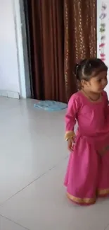 Toddler in pink traditional dress, standing indoors.