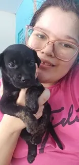 Cute black puppy with owner in pink shirt.