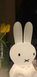 White rabbit night light with yellow tulips in a vase on a table.