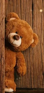 Cute teddy bear peeking from a rustic wooden background in cozy brown tones.